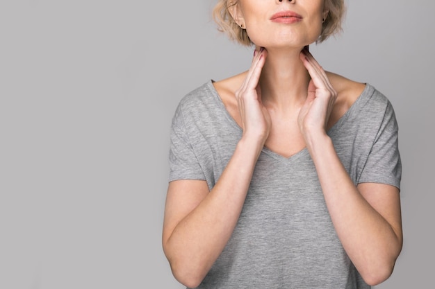 Mujer comprobando la glándula tiroides por sí misma. Cerca de mujer en camiseta blanca tocando el cuello con una mancha roja. El trastorno de la tiroides incluye bocio, hipertiroidismo, hipotiroidismo, tumor o cáncer. Cuidado de la salud.