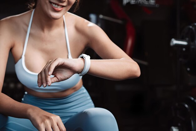 Mujer comprobando la hora y usando el teléfono inteligente ejercicio entrenamiento en el gimnasio fitness descansar relajarse después del entrenamiento deporte con pesas