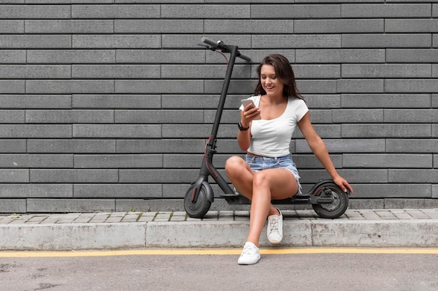 Foto mujer comprobando su teléfono inteligente mientras está sentado en scooter eléctrico