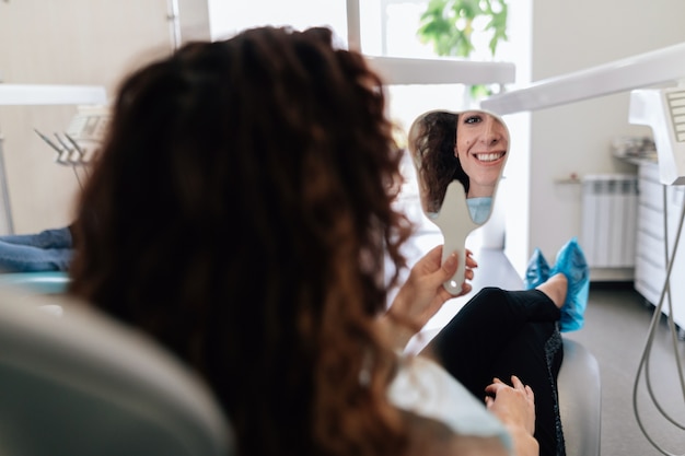 Mujer comprobando sus dientes en el espejo al dentista