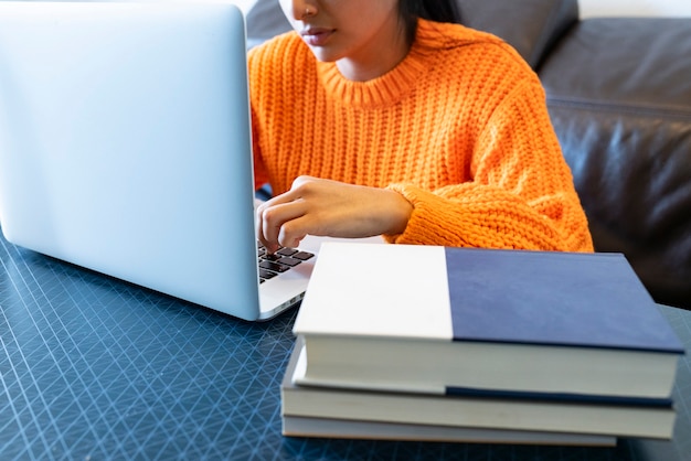 Mujer con computadora y libros en casa trabajando