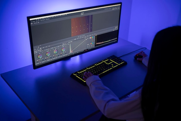 Una mujer se concentra en tareas de edición de video en su computadora con software profesional en una habitación iluminada por el sutil resplandor de la pantalla