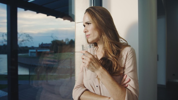 Mujer concentrada que se queda cerca de la ventana panorámica Mujer bonita esperando al hombre