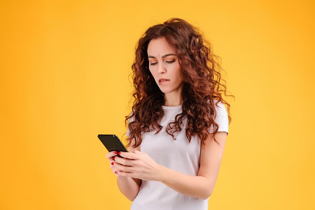 Mujer concentrada que usa su teléfono móvil aislado sobre fondo amarillo