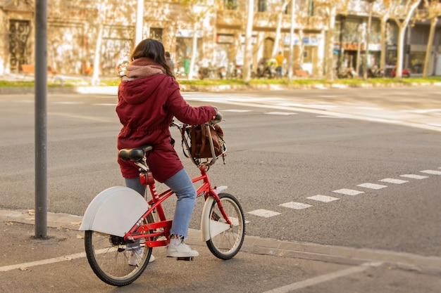 Mujer conduciendo bicicleta roja y blanca en una calle de una ciudad en un día soleado