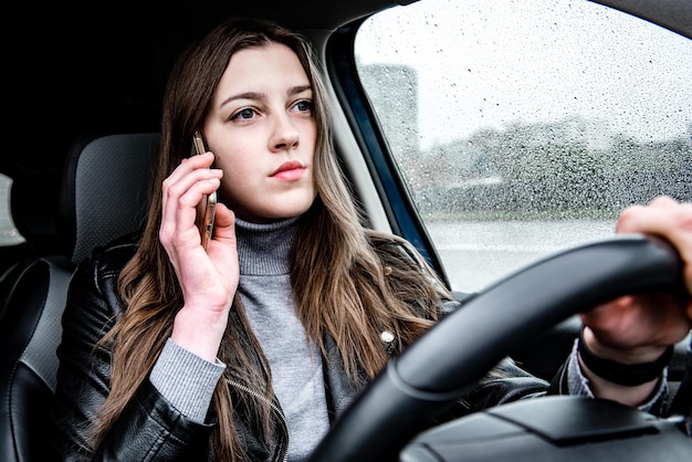 Mujer conduciendo coche y hablando por celular en malas condiciones climáticas.