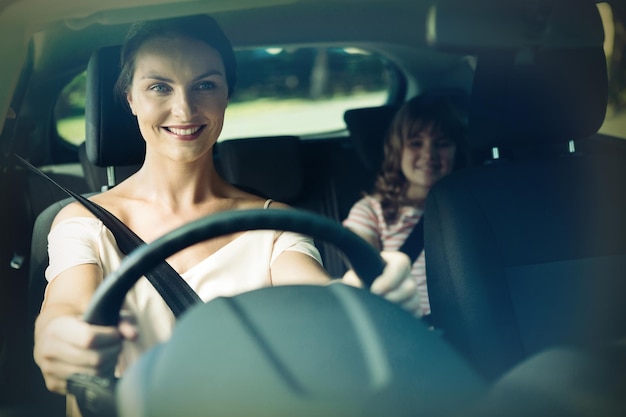 Mujer conduciendo un coche mientras su hija está sentada en el asiento trasero del coche