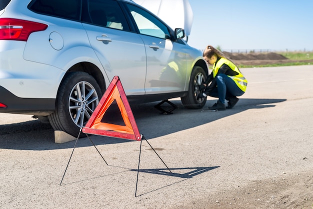 Mujer conductora cambiando rueda dañada en la carretera