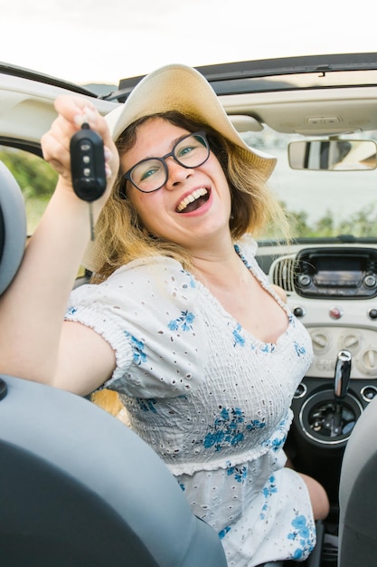 Mujer conductora de coche sonriendo mostrando las llaves del coche nuevo y el coche Mujer conduciendo cabrio alquilado en vacaciones de verano