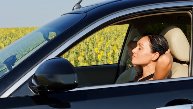 Mujer conductora descansando detrás del volante con las manos levantadas detrás de la cabeza mientras toma un descanso para refrescarse durante un largo viaje