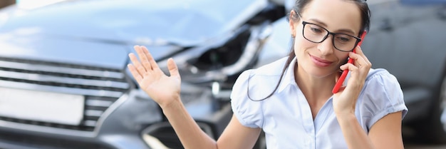 La mujer conductora está hablando por teléfono frente a un automóvil roto que informa el concepto de accidente automovilístico