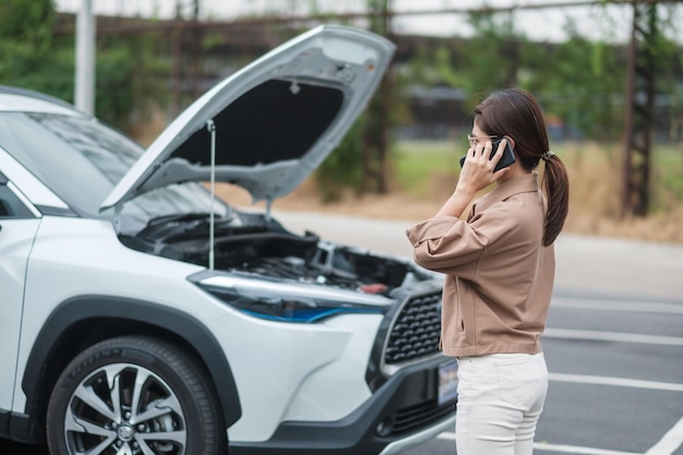 Mujer conductora que usa el teléfono móvil durante la avería del automóvil problemático o el automóvil roto en el concepto de servicio y mantenimiento del seguro del vehículo de carretera