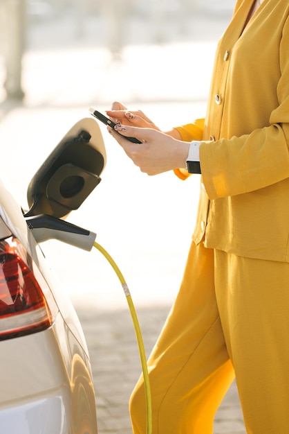 La mujer conecta un coche eléctrico al cargador y ajusta el proceso de carga de la batería del coche