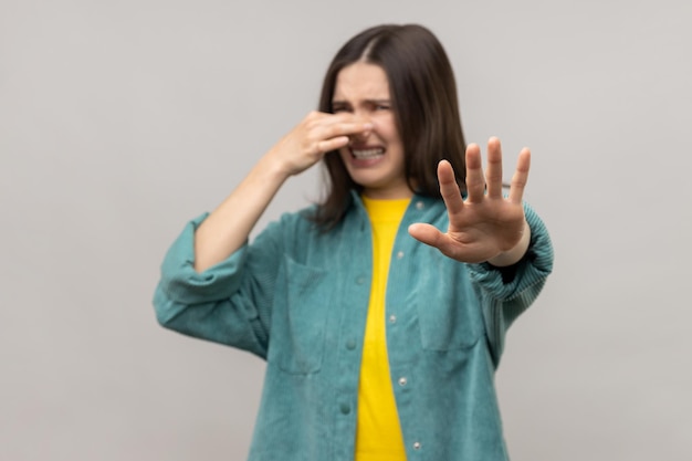 Mujer confundida pellizcando la nariz para contener la respiración y mostrando un gesto de parada disgustado por el olor desagradable