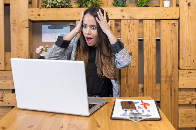 Foto mujer conmocionada leyendo información inesperada en su portátil