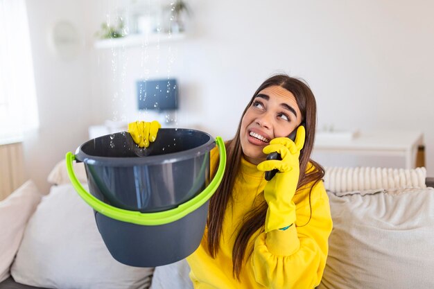Mujer conmocionada llamando al fontanero mientras recoge el agua que se filtra del techo usando utensilios