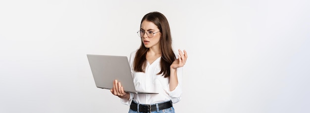 Mujer conmocionada mirando la pantalla del portátil confundida atónita por algo en la computadora de pie sobre blanco b