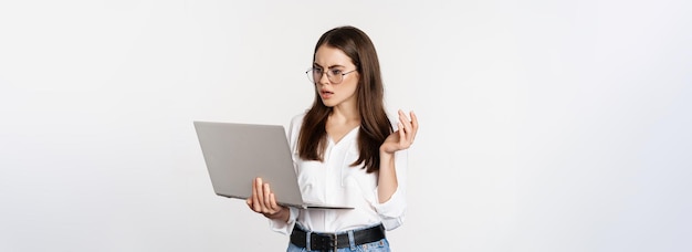 Foto mujer conmocionada mirando la pantalla del portátil confundida atónita por algo en la computadora de pie sobre blanco b