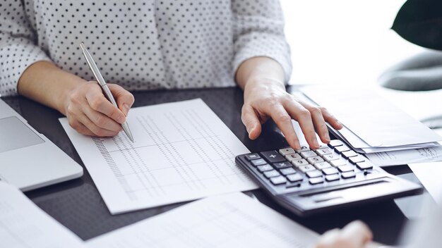 Mujer contable usando una calculadora y una computadora portátil mientras cuenta los impuestos con un cliente o un colega Asesora financiera del equipo de auditoría empresarial