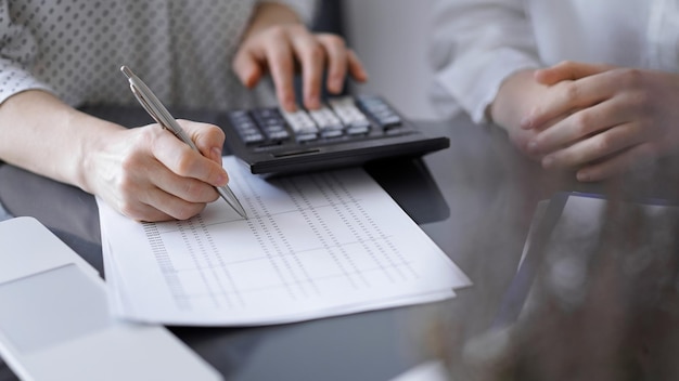 Mujer contable usando una calculadora y una computadora portátil mientras cuenta los impuestos para un cliente.