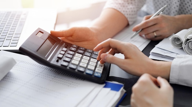 Mujer contable usando una calculadora y una computadora portátil mientras cuenta los impuestos para un cliente.