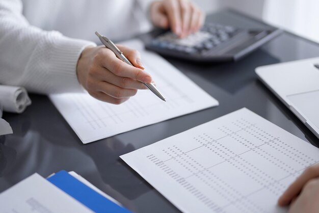 Mujer contadora que usa una calculadora y una computadora portátil mientras cuenta los impuestos para un cliente. Conceptos de auditoría empresarial