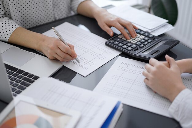 Mujer contadora que usa una calculadora y una computadora portátil mientras cuenta los impuestos con un cliente o un colega. Equipo de auditoría empresarial, asesor financiero