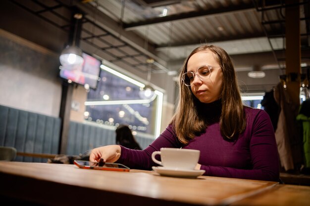 Foto mujer contemplando mientras sostiene un teléfono inteligente en una cafetería