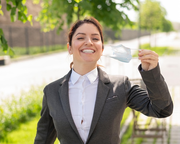 Foto una mujer contenta camina al aire libre mientras mantiene una distancia social una oficinista sonriente disfruta de la libertad de quitarse la máscara el coronavirus es derrotado el final de la jornada laboral