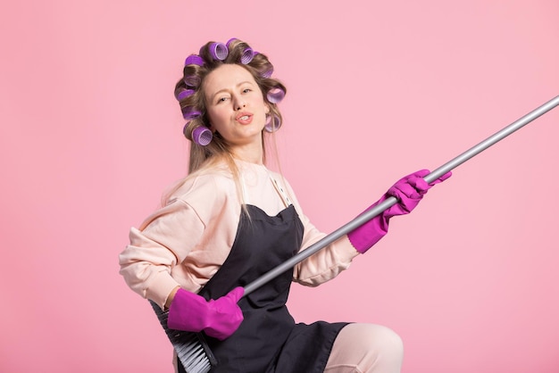 Una mujer contenta felizmente juega tontamente mientras limpia toca la escoba para barrer el piso como una guitarra