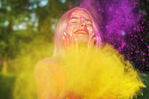 Mujer contenta posando de pie en una nube de pintura amarilla y violeta