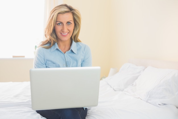 Mujer contenta sentado en la cama usando su computadora portátil