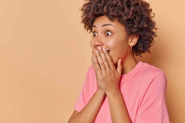 Mujer contras boca nota algo increíble mira fijamente sorprendida viste camiseta casual aislado en beige con espacio de copia para su anuncio