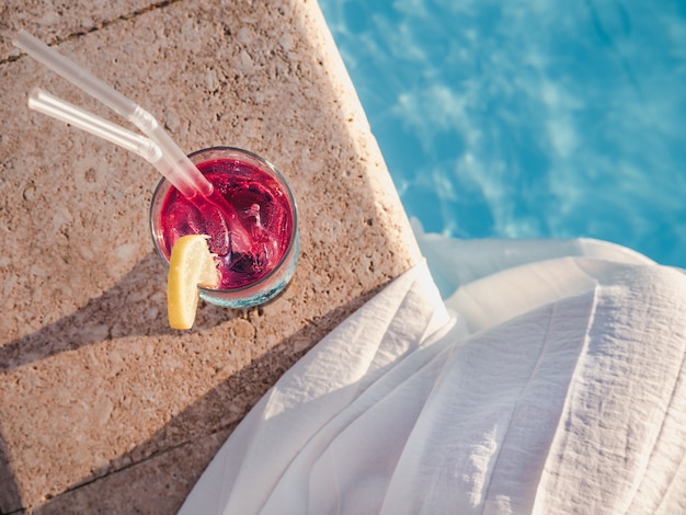 Mujer con copa de cóctel junto a la piscina. Vista superior