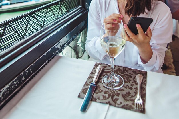 Mujer con una copa de vino sentada en el restaurante mirando el teléfono