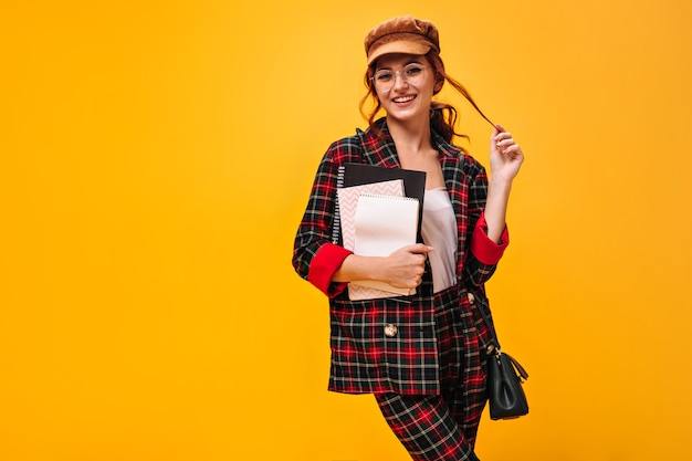 Mujer coqueta en traje de cuadros posa con cuadernos