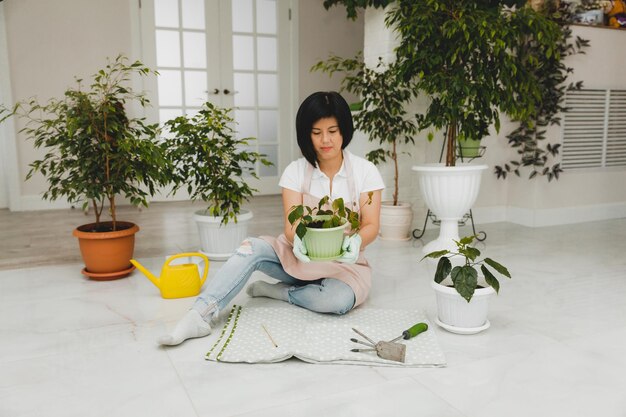 Una mujer coreana con un delantal cuida las plantas y las flores en una maceta. Jardinería y floricultura doméstica.