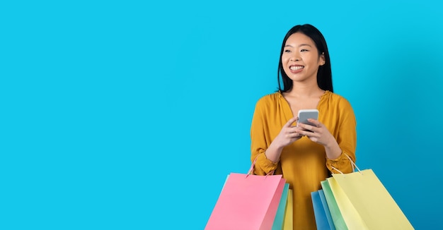 Mujer coreana feliz con bolsas de compras usando espacio de copia de teléfono inteligente