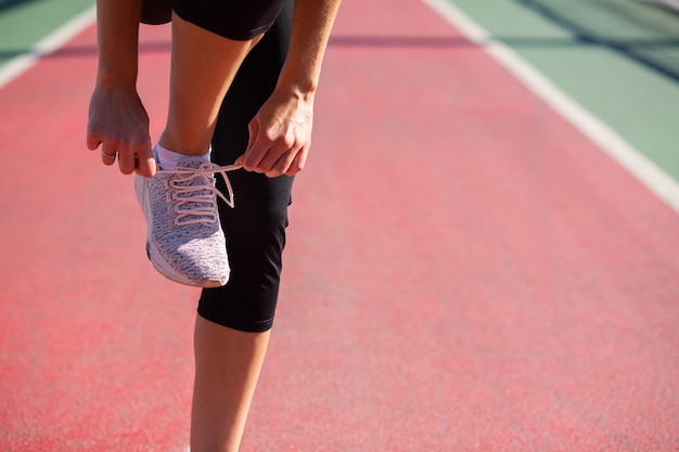 Mujer corredor atlético atar cordones de los zapatos en la pista deportiva en un día soleado. Espacio para texto