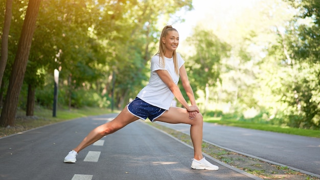 Mujer corredor estirar las piernas antes de hacer ejercicio en el parque de verano por la mañana