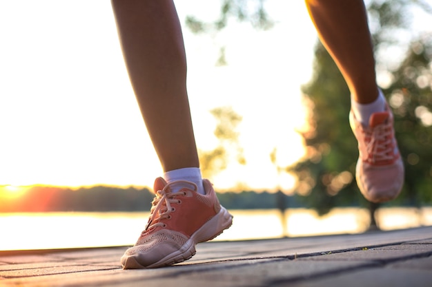 Mujer corredor piernas y zapatos en acción en la carretera al aire libre al atardecer.