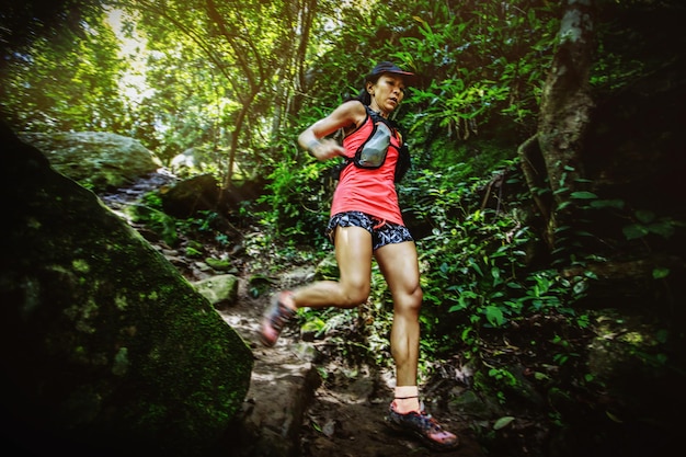 Mujer corredora de maratón de ultra trail corriendo cuesta abajo a través de la selva tropical