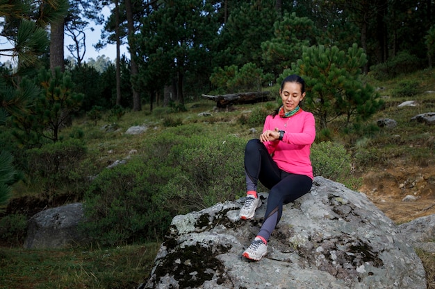 Mujer corredora usando su reloj inteligente despues de correr sentada en la orilla del lago