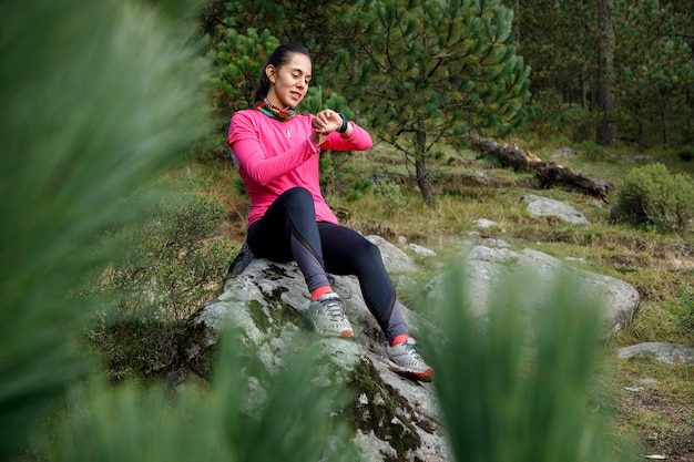 Mujer corredora usando su reloj inteligente despues de correr sentada en la orilla del lago