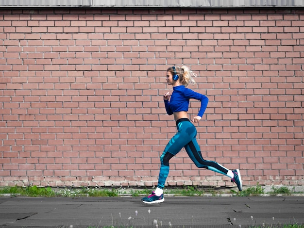 Mujer corriendo al aire libre en un fondo de pared de ladrillo de día soleado