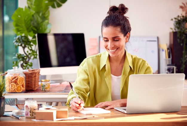 Mujer corriendo negocios en línea haciendo velas boutique en casa trabajando en la computadora portátil