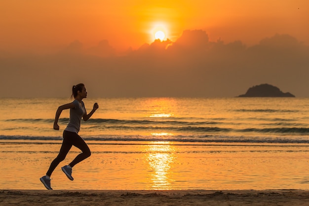 Mujer corriendo en la playa al amanecer con agua y olas de fondo.