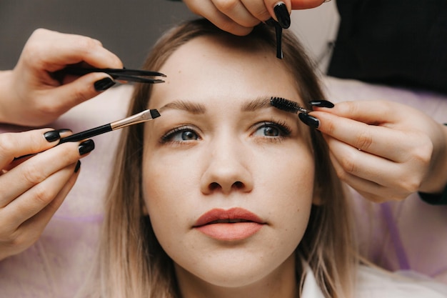 Una mujer corrige la forma de sus cejas en un salón de belleza 4 manos corrigen las cejas