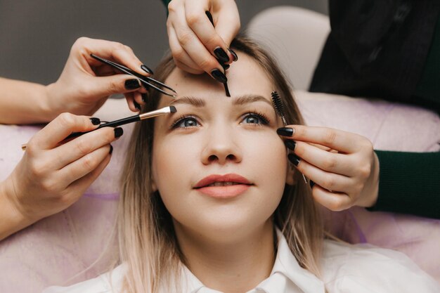 Una mujer corrige la forma de sus cejas en un salón de belleza 4 manos corrigen las cejas