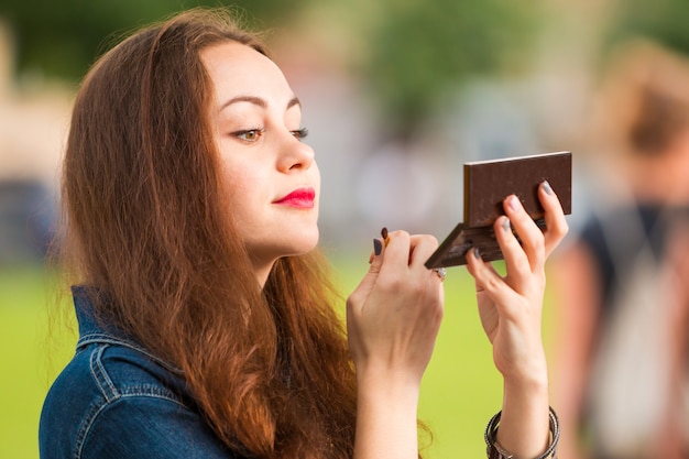 Foto mujer corrige maquillaje con lápiz labial rojo en el parque